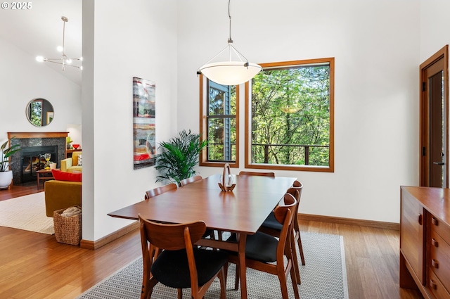 dining area with baseboards, a glass covered fireplace, wood finished floors, and a towering ceiling