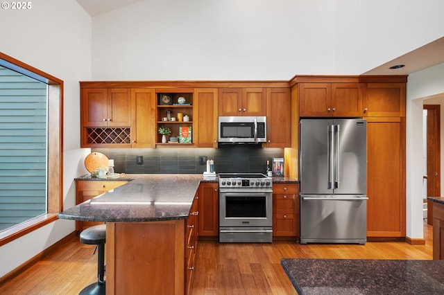 kitchen featuring appliances with stainless steel finishes, decorative backsplash, wood finished floors, and a towering ceiling