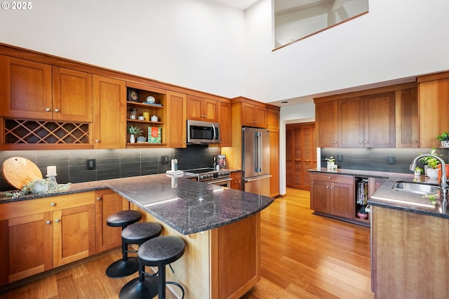kitchen with brown cabinetry, a kitchen breakfast bar, high quality appliances, a sink, and light wood-style flooring