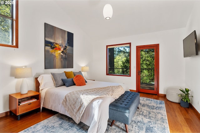 bedroom featuring baseboards, wood finished floors, vaulted ceiling, and access to exterior