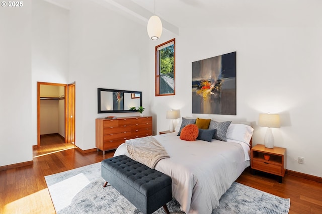 bedroom with wood finished floors, baseboards, lofted ceiling, and a spacious closet