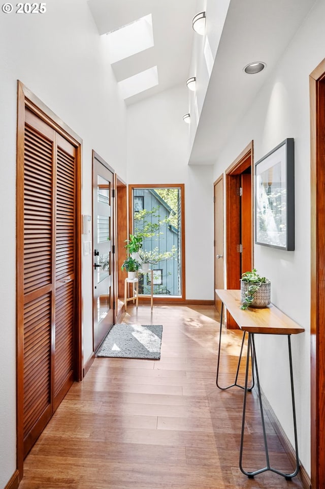 interior space featuring a skylight, baseboards, light wood-style floors, and high vaulted ceiling