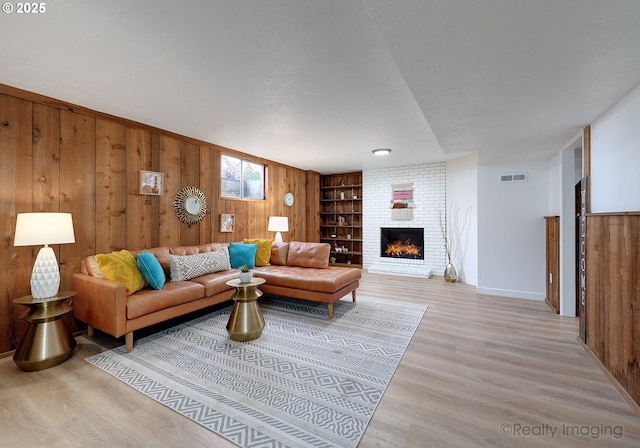 living area featuring wood walls, light wood-style flooring, a brick fireplace, and built in shelves