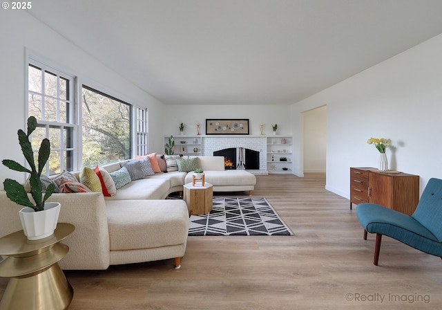 living room with a brick fireplace, baseboards, and light wood finished floors