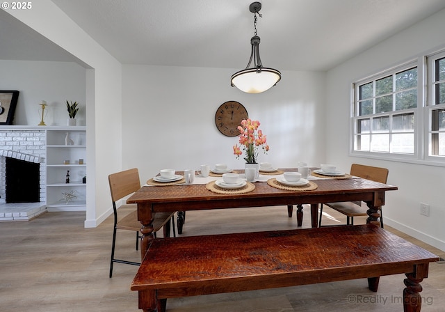 dining space featuring a fireplace, light wood-style flooring, and baseboards