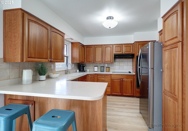 kitchen featuring electric stovetop, freestanding refrigerator, a peninsula, under cabinet range hood, and a sink