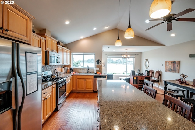 kitchen with decorative light fixtures, appliances with stainless steel finishes, a kitchen breakfast bar, dark stone counters, and light hardwood / wood-style floors