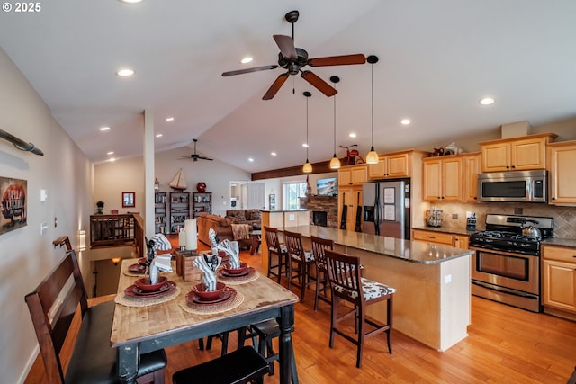 kitchen featuring pendant lighting, lofted ceiling, stainless steel appliances, a kitchen island, and light wood-type flooring