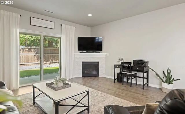 living area featuring a tile fireplace, wood finished floors, visible vents, and baseboards