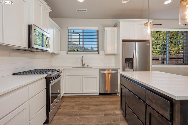 kitchen with stainless steel appliances, a sink, white cabinetry, visible vents, and pendant lighting