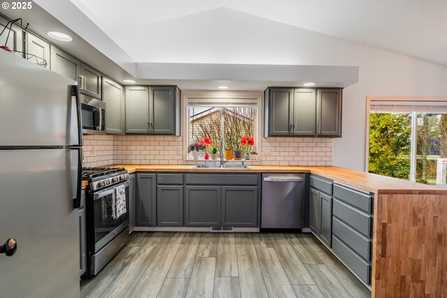 kitchen with lofted ceiling, wood counters, stainless steel appliances, sink, and backsplash