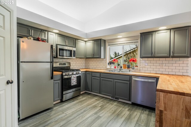 kitchen featuring wood counters, appliances with stainless steel finishes, decorative backsplash, light hardwood / wood-style flooring, and sink