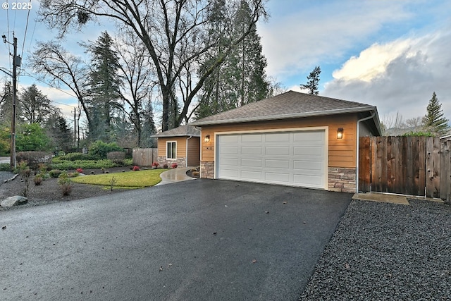 view of front of house with a garage, stone siding, driveway, and fence