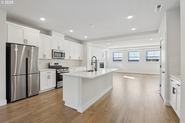 18315 SW Silvertip St, Beaverton, OR 97007 - kitchen with stainless steel appliances, a sink, tasteful backsplash, white cabinetry, and light wood-style flooring