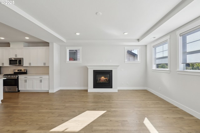 18315 SW Silvertip St, Beaverton, OR 97007 - unfurnished living room with baseboards, light wood-style floors, a glass covered fireplace, a tray ceiling, and recessed lighting