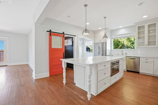 kitchen with a center island, white cabinets, hanging light fixtures, a barn door, and appliances with stainless steel finishes