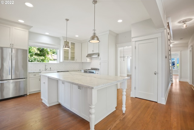 kitchen with stainless steel refrigerator, light stone counters, white cabinets, and a kitchen island