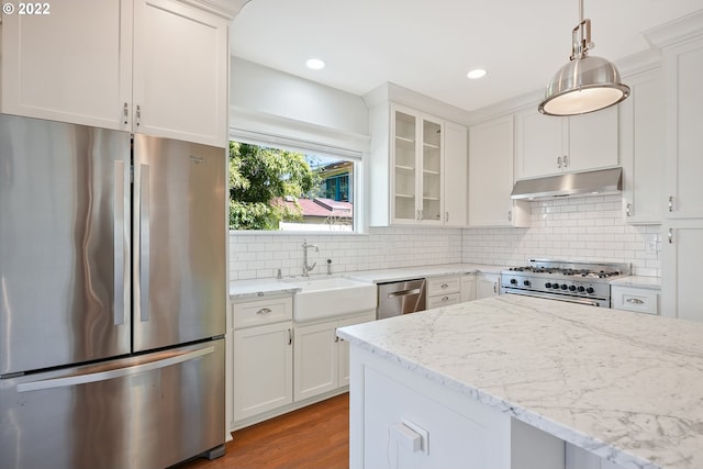 kitchen with light stone countertops, appliances with stainless steel finishes, sink, white cabinets, and hanging light fixtures