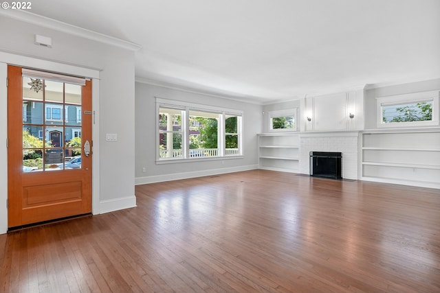 unfurnished living room featuring built in shelves, a brick fireplace, ornamental molding, and hardwood / wood-style floors