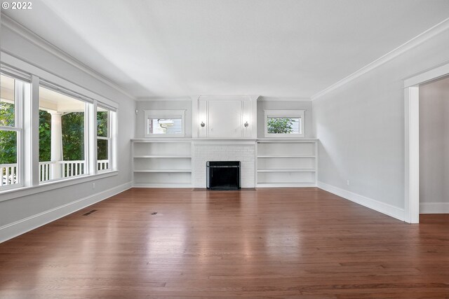 unfurnished living room featuring built in shelves, crown molding, dark wood-type flooring, and a brick fireplace