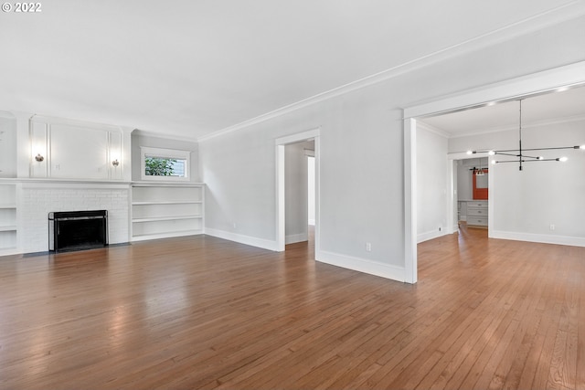 unfurnished living room with a notable chandelier, wood-type flooring, ornamental molding, and a brick fireplace