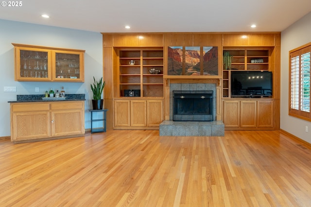 unfurnished living room featuring recessed lighting, bar, light wood-style flooring, and a tiled fireplace