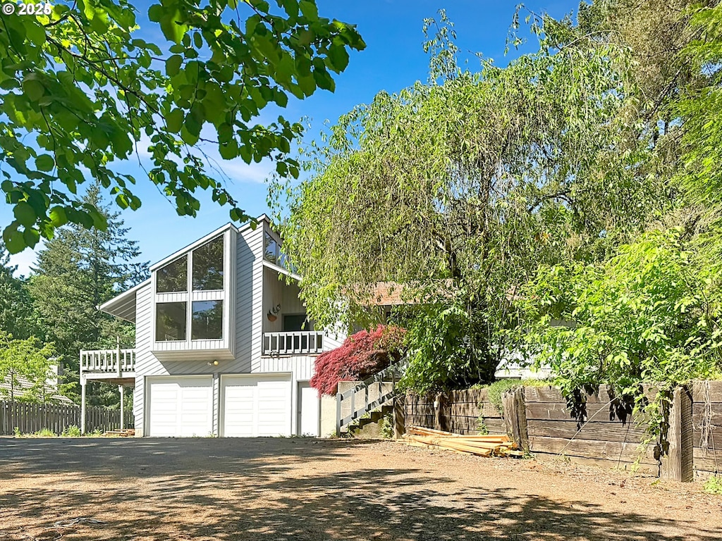 view of front of house featuring stairway, fence, a garage, and dirt driveway