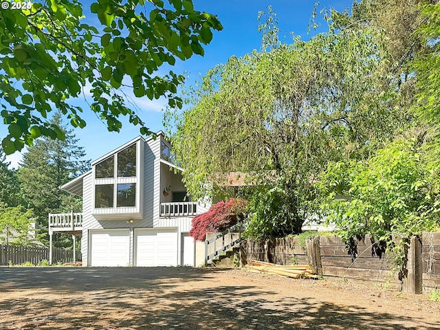 view of front of house featuring stairway, fence, a garage, and dirt driveway