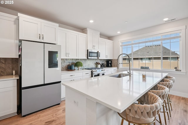 12545 SW Palermo St, Wilsonville, OR 97070 - kitchen featuring stainless steel appliances, a sink, decorative backsplash, light wood-style floors, and a kitchen breakfast bar