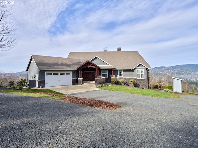 view of front facade with a garage, driveway, stone siding, and a mountain view