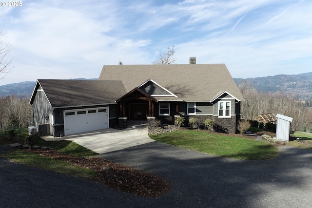 view of front of home featuring driveway, a garage, stone siding, central air condition unit, and a mountain view