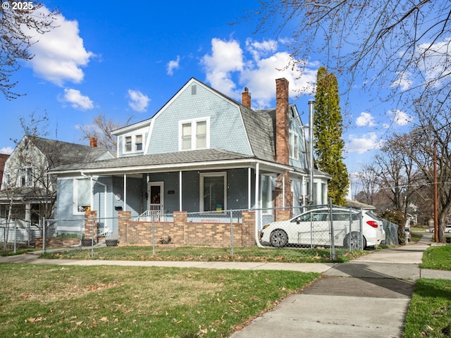 colonial inspired home featuring a porch, brick siding, a gambrel roof, and a fenced front yard