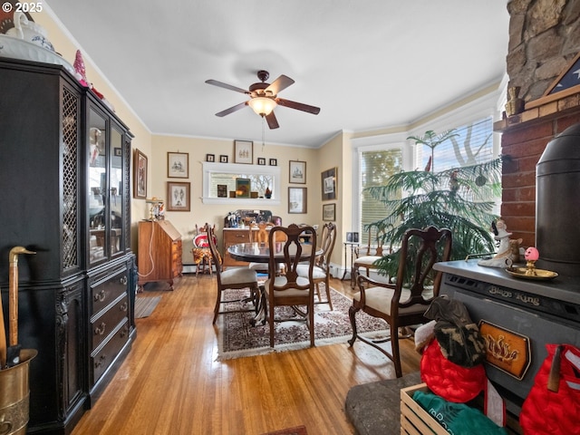 dining space featuring crown molding, light wood-style floors, ceiling fan, and a wood stove