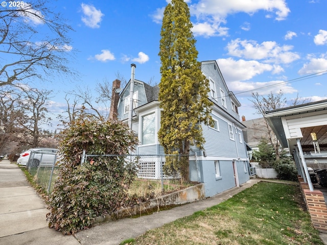 view of side of home with a yard, fence, and a chimney