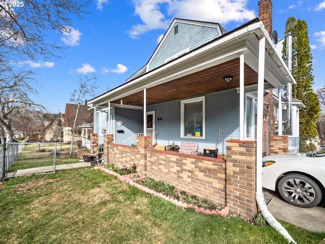 view of front facade with a front lawn, fence, a porch, a chimney, and a gate