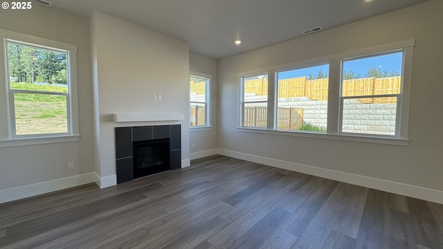 unfurnished living room featuring baseboards, visible vents, wood finished floors, and a healthy amount of sunlight
