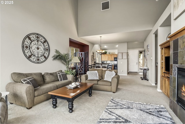 carpeted living room with a towering ceiling, a tiled fireplace, and a notable chandelier