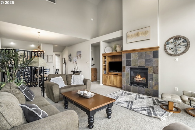 carpeted living room with a towering ceiling, a tiled fireplace, built in features, and a notable chandelier