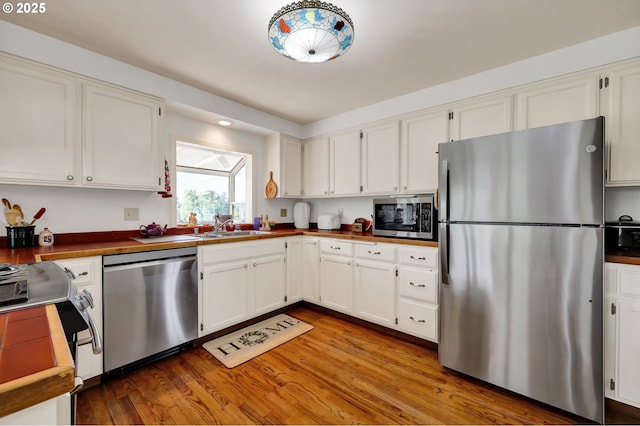 kitchen with a sink, white cabinets, stainless steel appliances, and wood finished floors