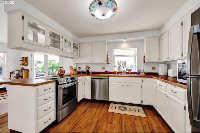 kitchen featuring a peninsula, glass insert cabinets, dark wood-type flooring, white cabinets, and stainless steel appliances