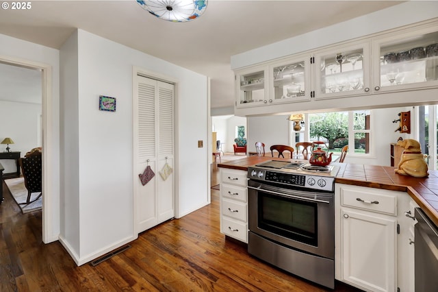 kitchen with dark wood-style flooring, visible vents, appliances with stainless steel finishes, glass insert cabinets, and tile counters
