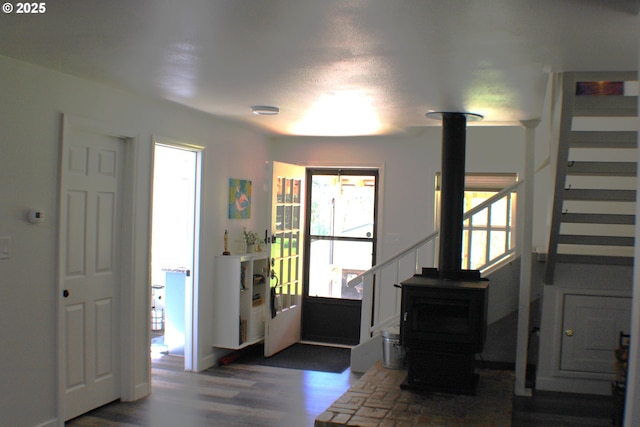 foyer with stairway, a wealth of natural light, a wood stove, and wood finished floors