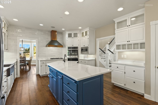 kitchen with appliances with stainless steel finishes, white cabinets, wall chimney range hood, and blue cabinetry