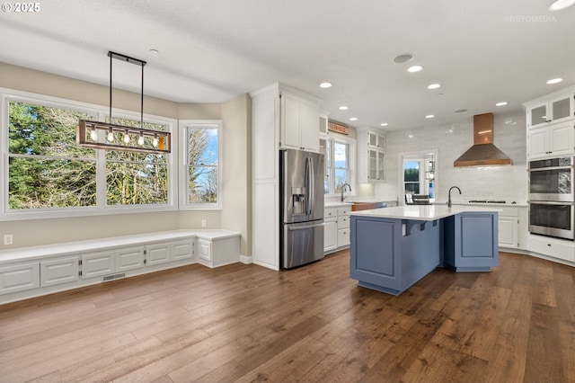 kitchen with stainless steel appliances, wall chimney exhaust hood, light countertops, and white cabinetry