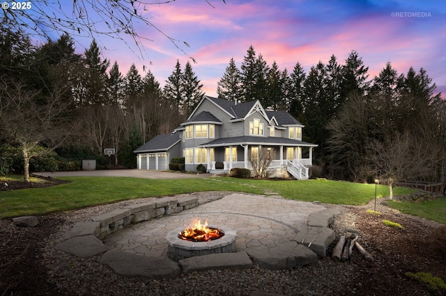 view of front of property featuring a porch, an outdoor fire pit, a garage, driveway, and a front yard