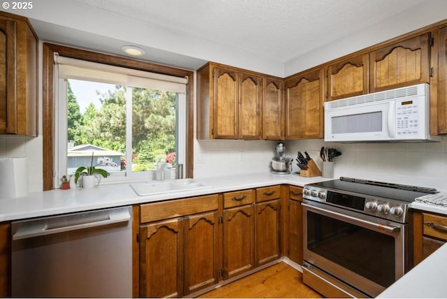 10701 SE Stevens Way, Happy Valley, OR 97086 - kitchen with appliances with stainless steel finishes, a sink, light countertops, brown cabinets, and a textured ceiling