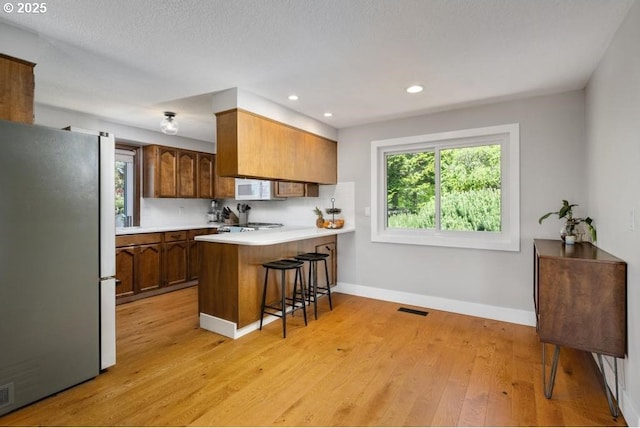 10701 SE Stevens Way, Happy Valley, OR 97086 - kitchen with freestanding refrigerator, light countertops, a peninsula, light wood-type flooring, and baseboards
