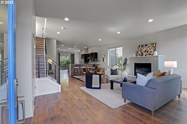 living area with stairs, wood-type flooring, recessed lighting, a fireplace with raised hearth, and baseboards