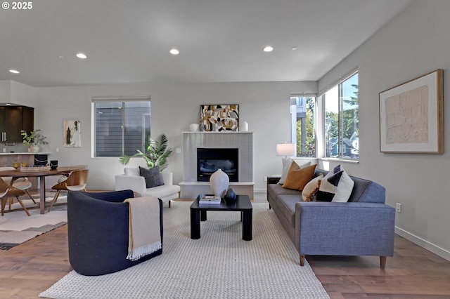 living room with wood finished floors, recessed lighting, a fireplace with raised hearth, and baseboards