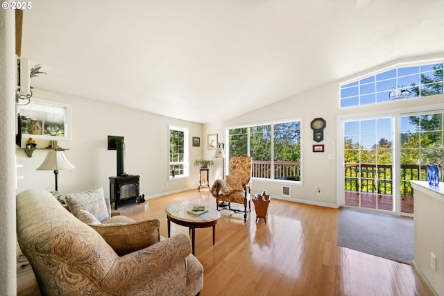 living room with light wood finished floors, a wood stove, baseboards, lofted ceiling, and visible vents